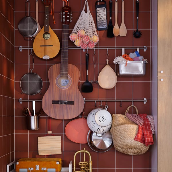 A tiled reddish-brown wall with various kitchen utensils, fruit, instruments, and other items hung on KUNGSFORS rails.