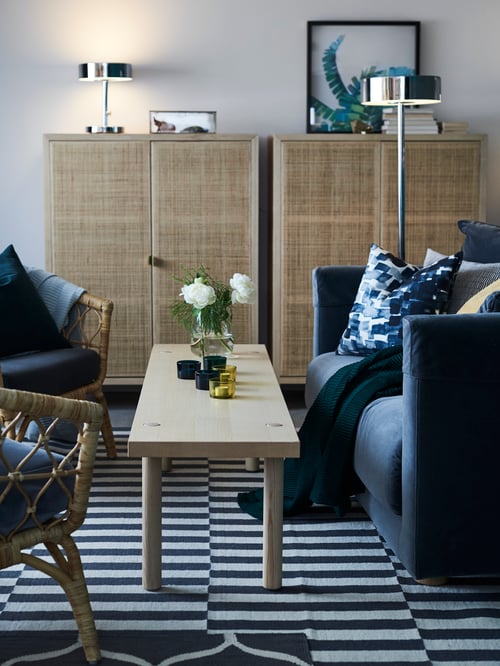 Living room with a flatwoven rug, a coffee table, a three-seat sofa., two beige cabinets, and an armchair with cushion.