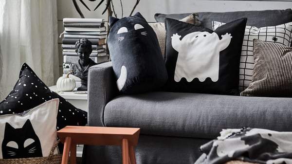 A black cat KUSTFYR soft toy cushion on a dark grey sofa for Halloween decoration