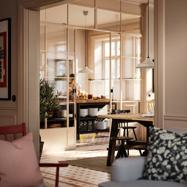 Part of an acacia SKOGSTA dining table with black legs is visible by a breakfast buffet area that is behind a glass wall.
