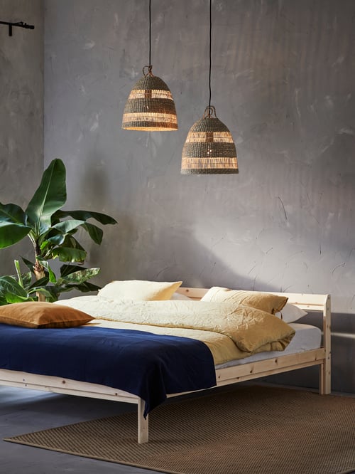 Bedroom with bed frame, duvet cover and pillowcases, cushion covers, green houseplant, pendant lamp shades, bedspread, rug.