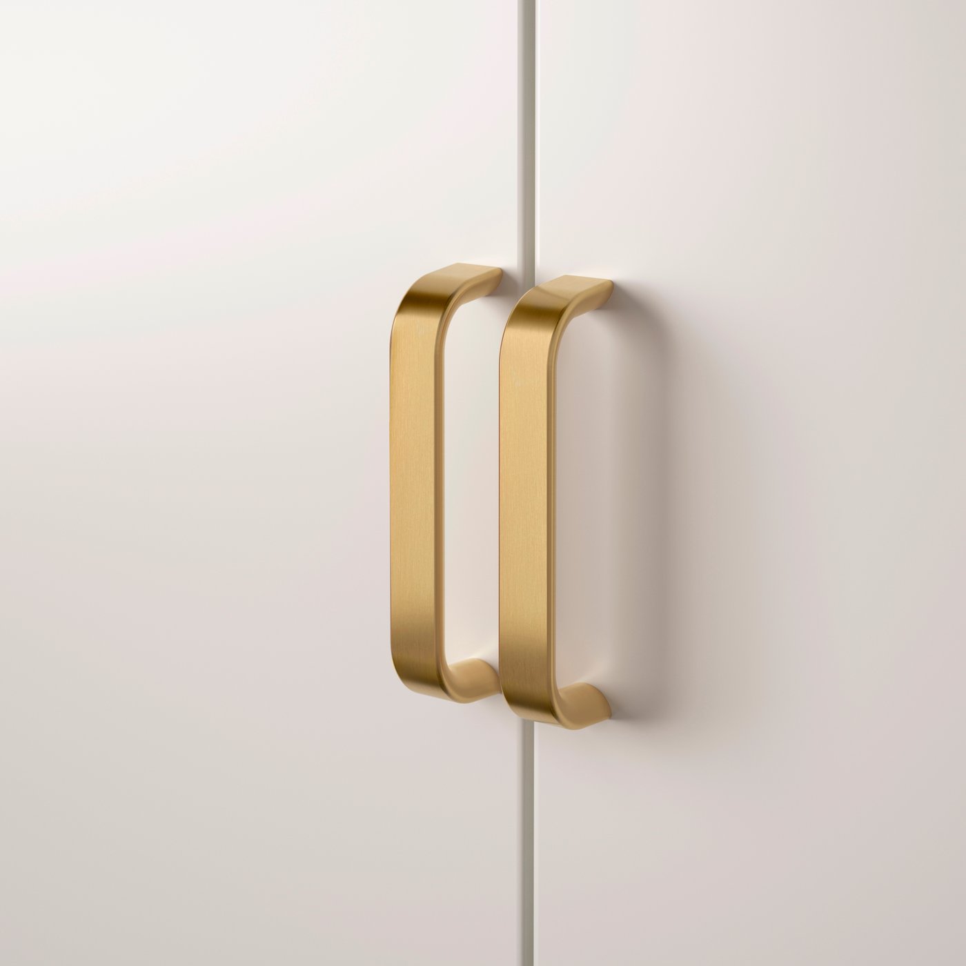 Två KALERUM handtag i mässingsfärg på en vit garderob.
