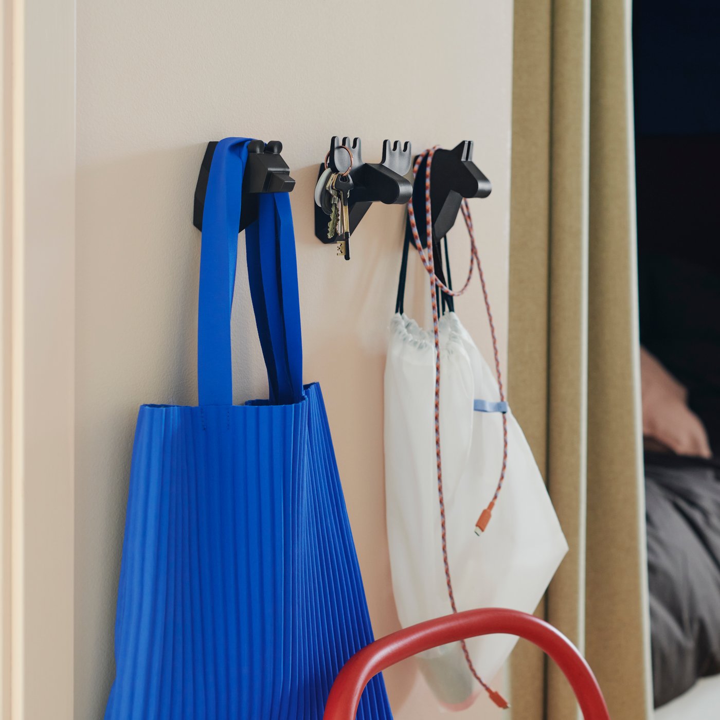 Three black FRÖSÅDD hooks, shaped like animal heads, are mounted on a wall with bags, keys and cables hanging on them.