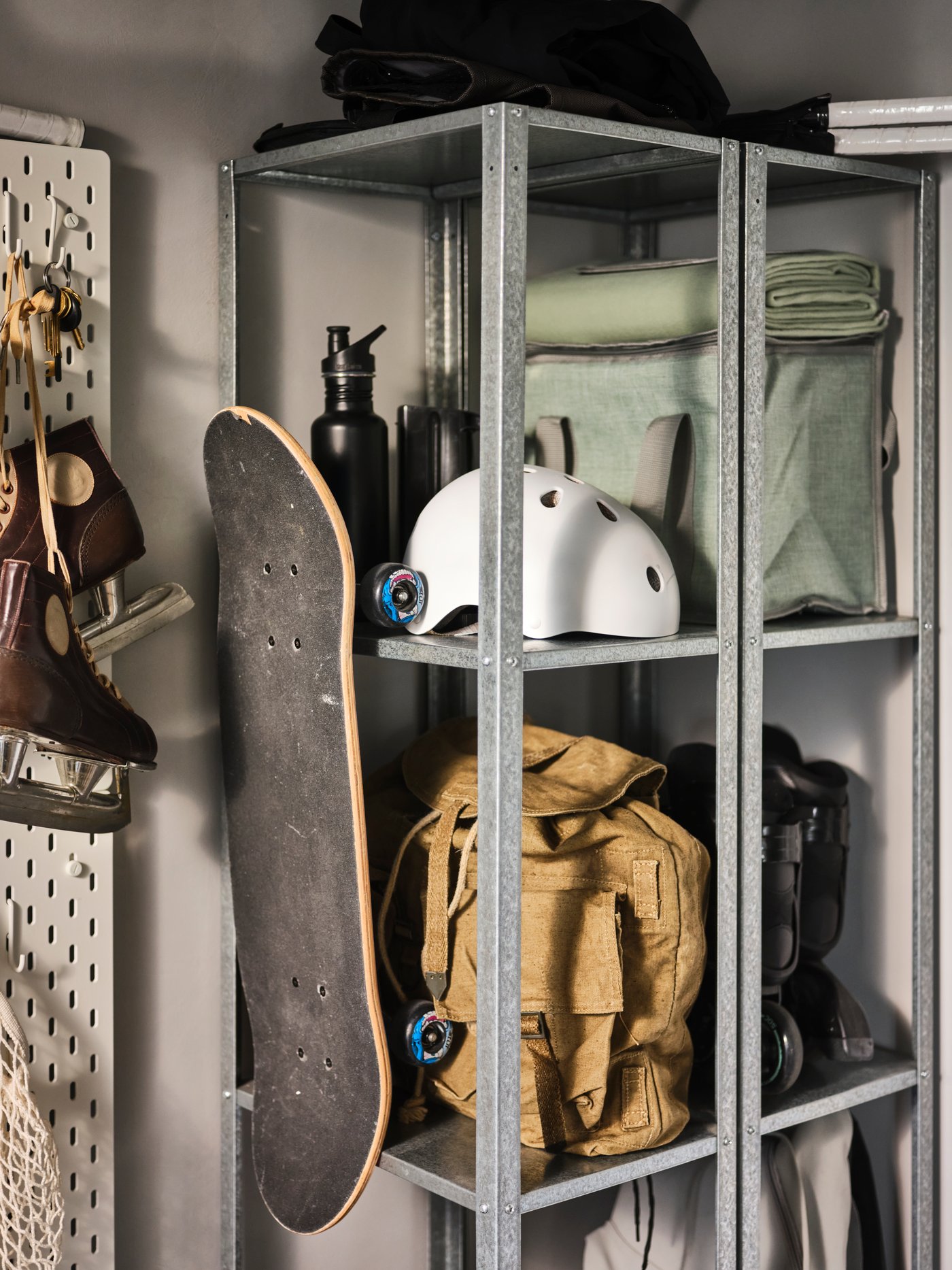 Une entrée avec deux étagères HYLLIS en métal où sont rangés une planche à roulettes, un sac à dos, un casque, une bouteille à eau et bien plus.
