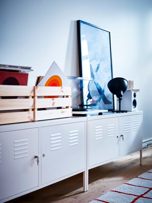 Workspace area with a frame, two wooden boxes, and a table uplighter placed on two cabinets, and a rug on the floor.