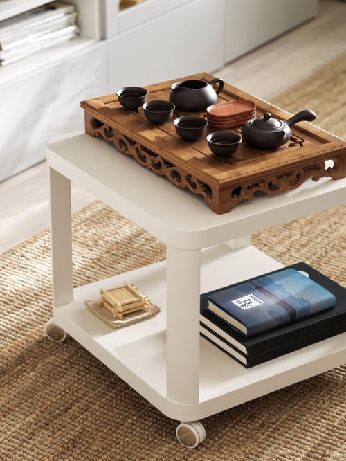 Living room featuring a white side table on castors on a rug, containing a board with teacups and pots, and books.