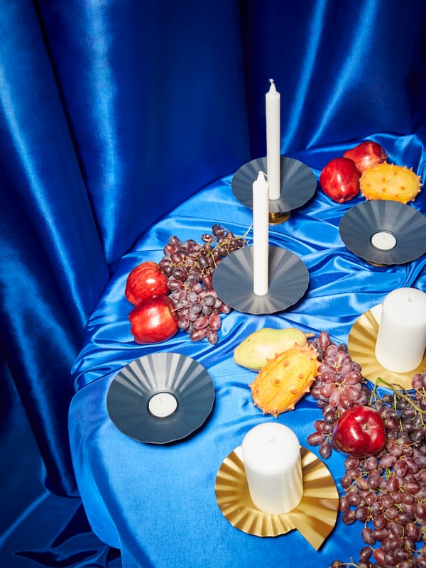 KARISMATISK Kerzen- oder Teelichthalter aus Metall in Blau/Goldfarben und goldfarbene Kerzenschalen stehen auf einem Tisch, der mit einem blauen Satinstoff bedeckt ist.   