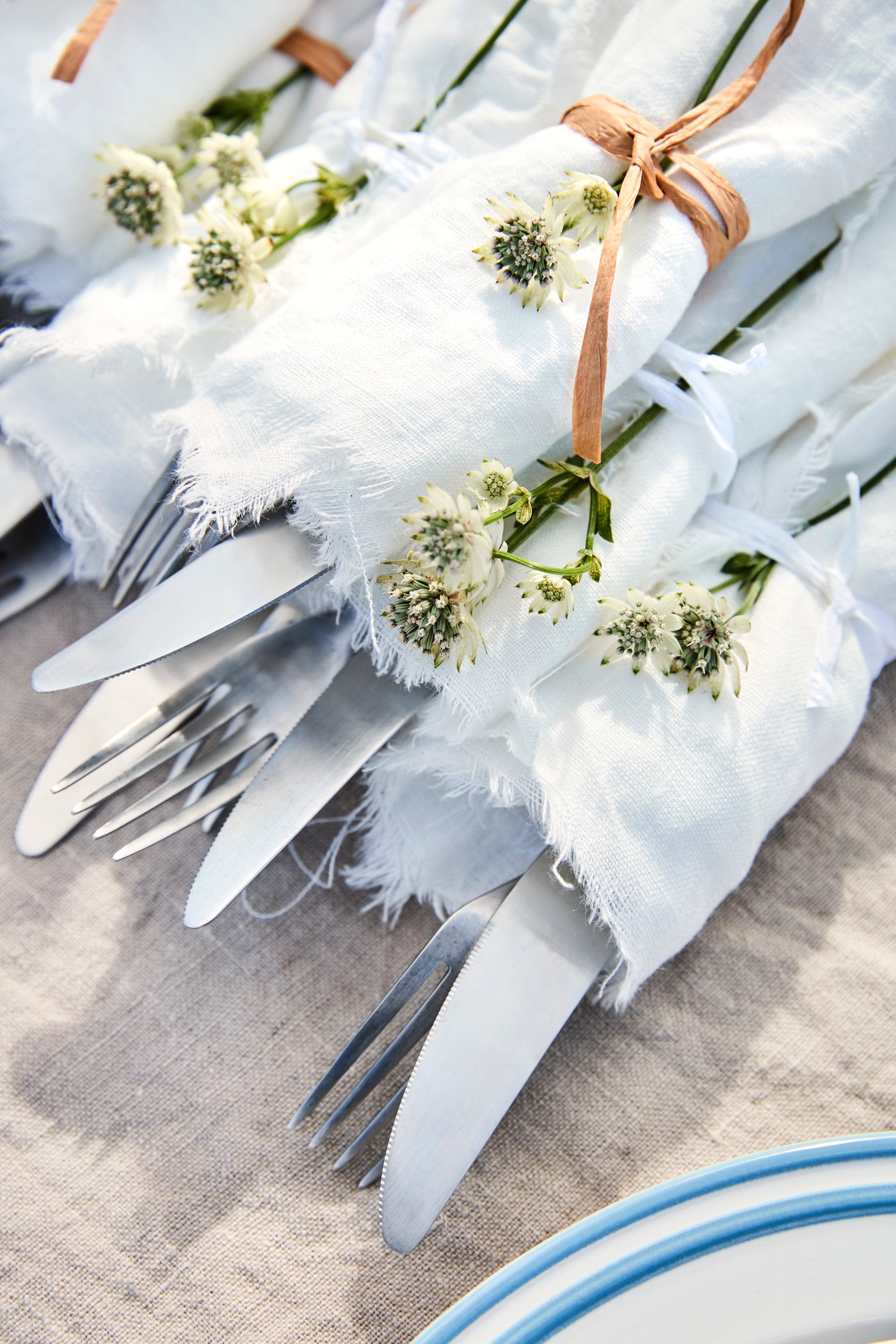 Bestik er rullet ind i stofservietter som er bundet med en snor, hvor der også sidder en blomst i. 