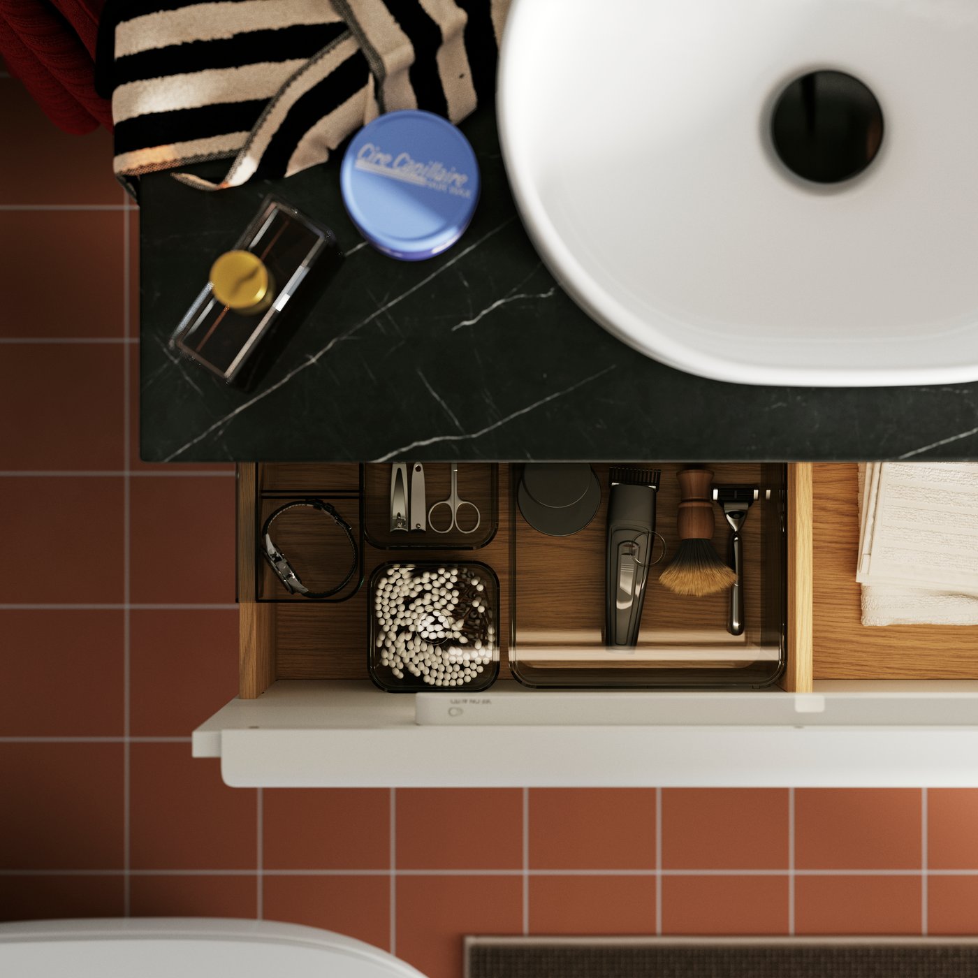 An open bathroom drawer displaying organised grooming tools and beauty items, with terracotta tiles visible below.