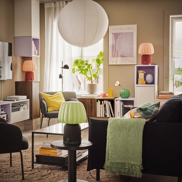 A light, colourful living room with plants, decoration and three KULGLASS Bluetooth speaker lamps scattered across the room.