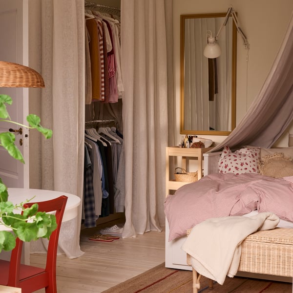 A room with a table to the left in the foreground and a bed to the right. A wardrobe solution with curtains in the back.