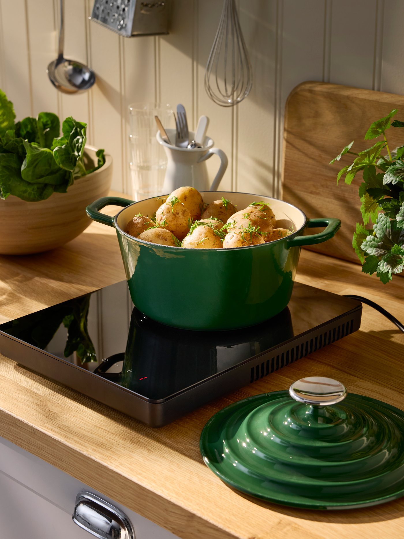 A kitchen with a black TILLREDA portable induction hob is cooking potatoes in a green pot on a wooden countertop.