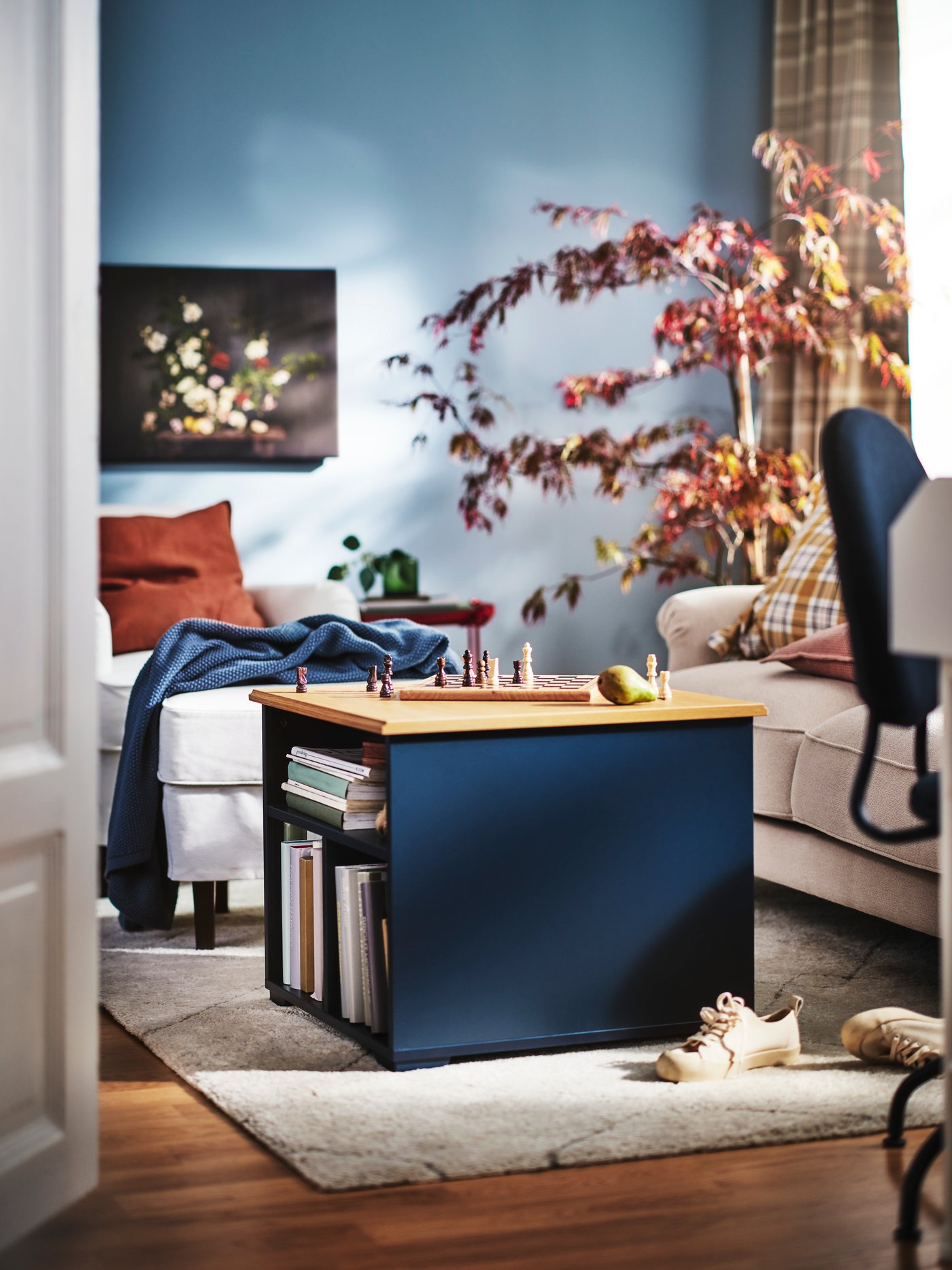 Ein schwarzblauer SKRUVBY Couchtisch steht in einem Wohnzimmer auf einem grauen flach gewebten VÄGNÄT Teppich vor einem ROCKSJÖN Hocker. 