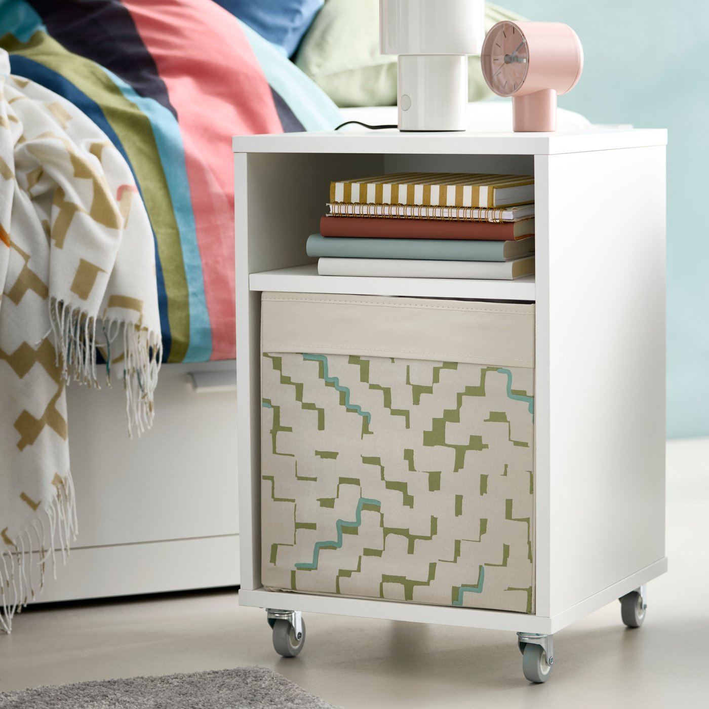 Close up of a white VIHALS bedside table with a DRÖNA box inside close to a BRIMNES day-bed.