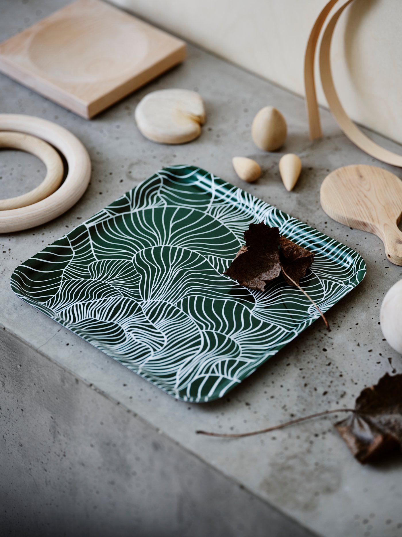 A dark green VINTERSNÖ tray with a white mushroom pattern is on a grainy stone surface with wooden ornaments and leaves.
