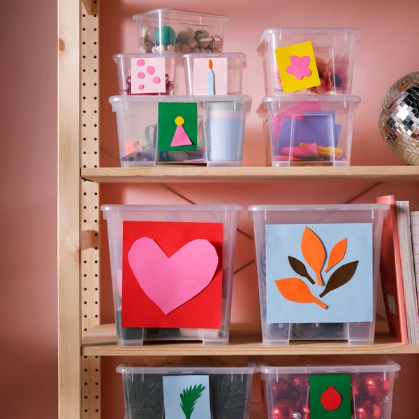 SAMLA storage boxes in different sizes, marked for different celebrations and holding ornaments, placed on wooden shelving.