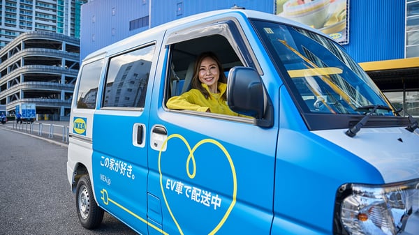 イケア店舗前で、EV配送車に乗ったコワーカーが笑顔で待機する、サステナブルな配達シーン。