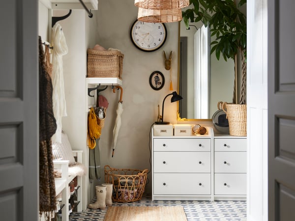  A hallway with beige walls, a coat rack and benches to the left and chests of drawers in front. Mix of decorations all over.