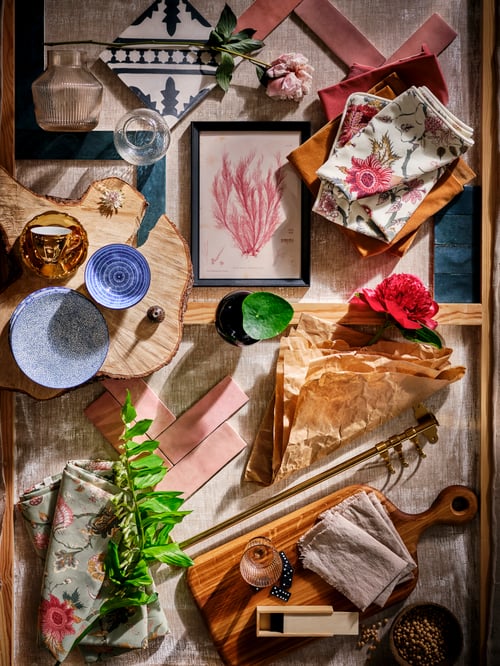 A mood board photographed from above including patterned ENTUSIASM side plates, pink tiles, wood, textiles, pink flowers and leaves.