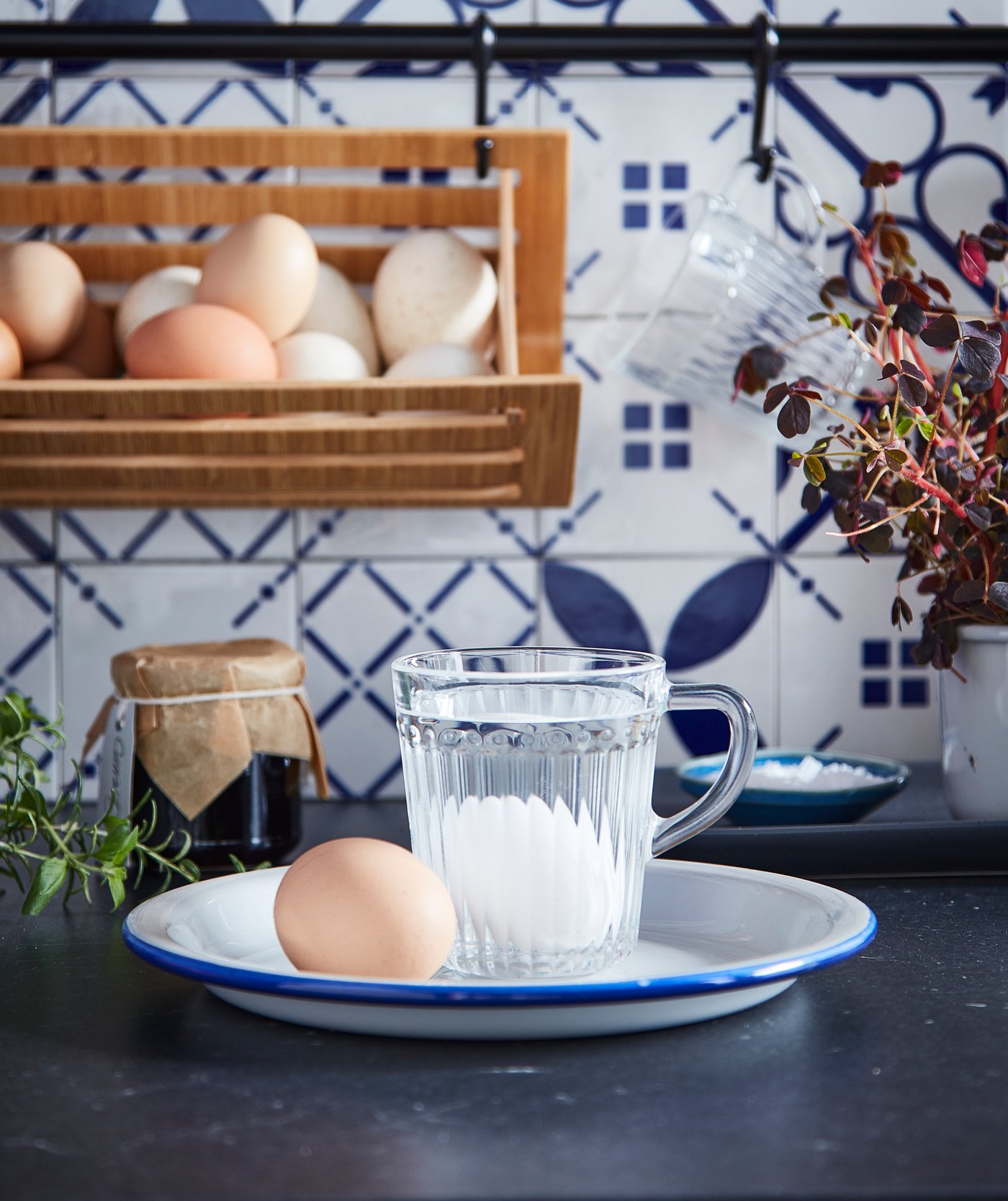 Eier auf einem Teller, eines davon liegt in DRÖMBILD Becher aus Klarglas im Wasser. Im Hintergrund ist ein Eierkorb zu sehen.