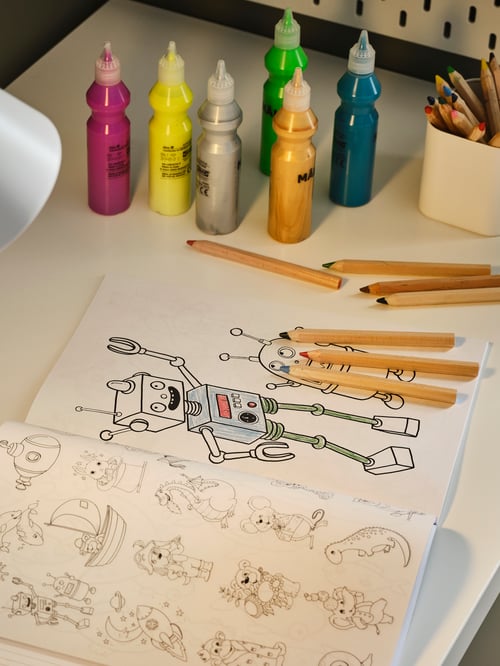 A desktop with an open, partly colourized MÅLA colouring book, assorted MÅLA glitter paint, and MÅLA coloured pencils.