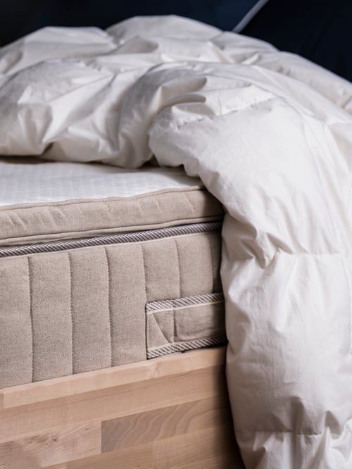 A VATNESTRÖM pocket sprung mattress with a TISTEDAL mattress pad on a wooden bed with a white duvet draped over it.
