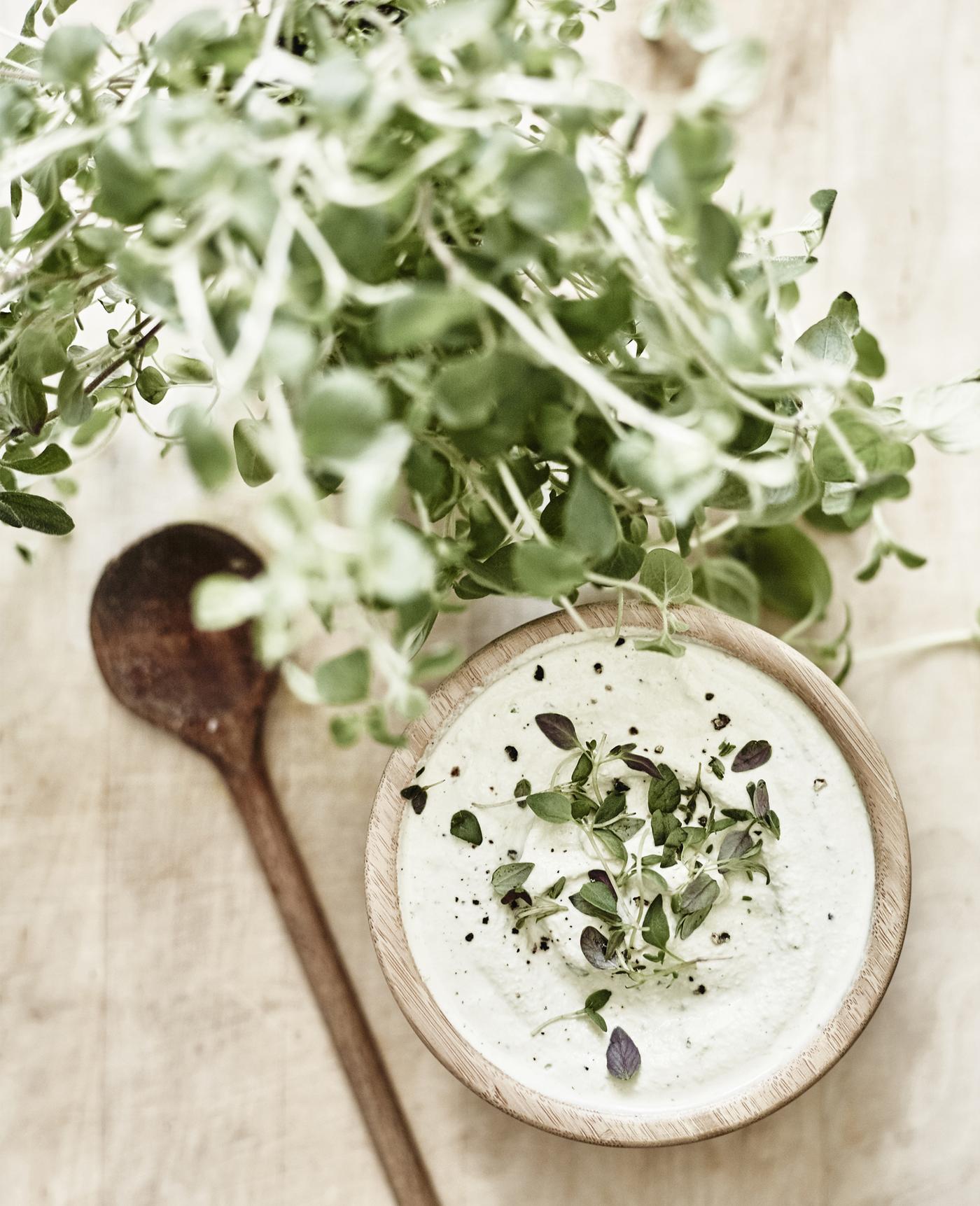 Holzschüssel mit cremigem Dip, garniert mit frischen Kräutern, daneben Holzlöffel und grünes Kräuterbündel.