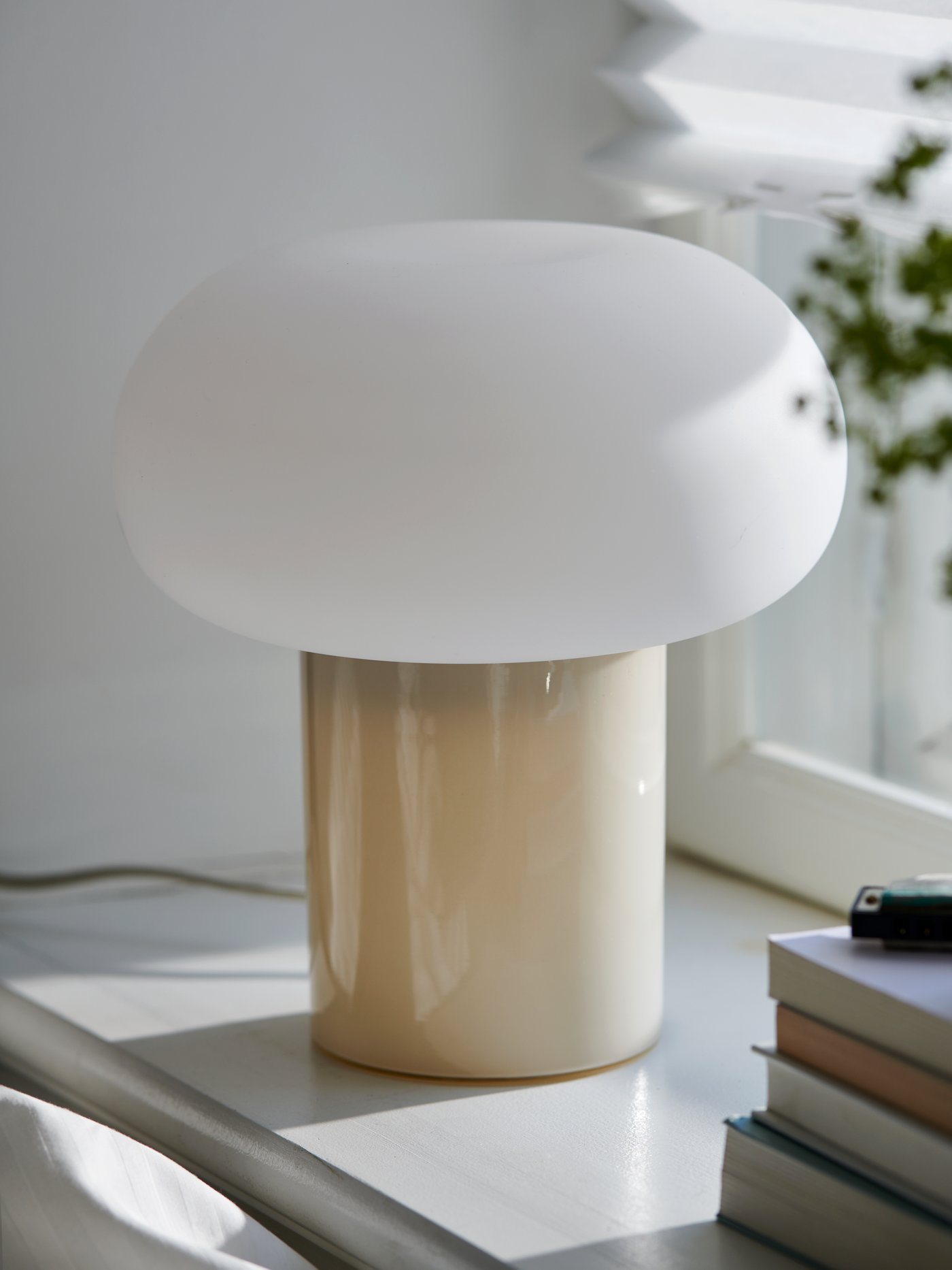 A beige/opal white glass DEJSA table lamp on the windowsill of a home office.