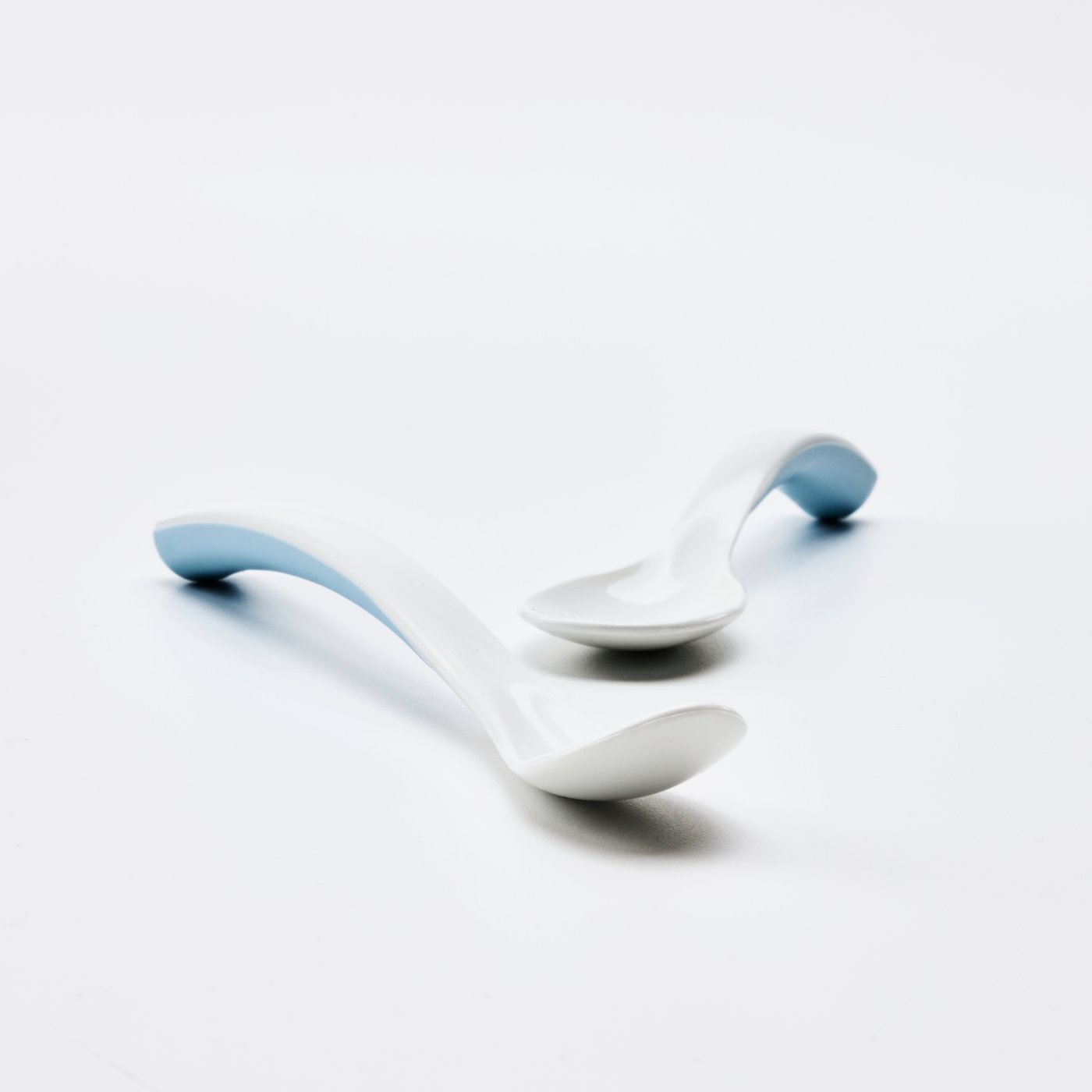 Niebiesko-biała łyżka do karmienia i łyżka dla dzieci i BÖRJA leżą na białej powierzchni w całkowicie białym otoczeniu.