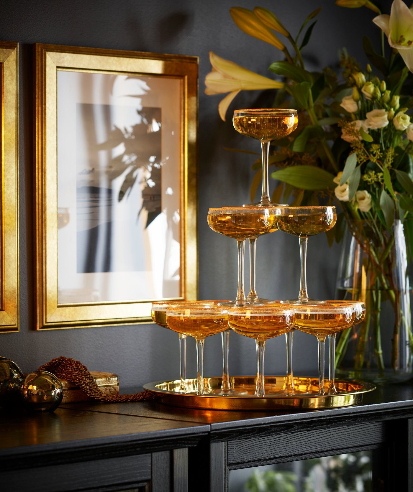 A champagne tower made of STORHET champagne coupes on a sideboard, set against a dark wall with gold photo frames in the living room.