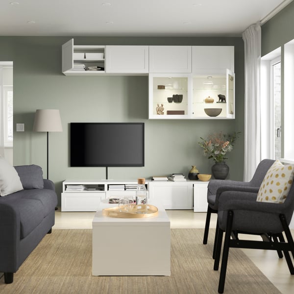 It is a cozy living room with green walls, a light blue HYLTARP sofa in front of a row of white BILLY bookshelves with OXBERG glass doors.