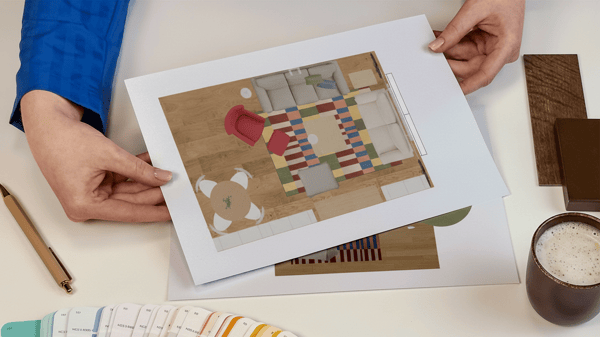Projektantka wnętrz IKEA prezentująca kartki z wydrukiem rzutu z góry zaprojektowanego pomieszczenia. Obok na blacie leży wzornik kolorów i próbki materiałów.