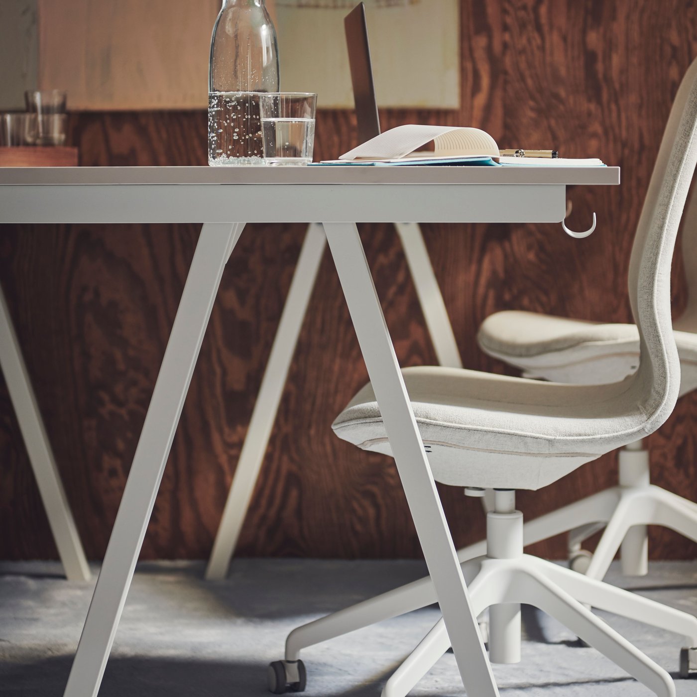 A beige HATTEFJÄLL office chair in front of a white TROTTEN desk with a water bottle, glass and notepad on top.
