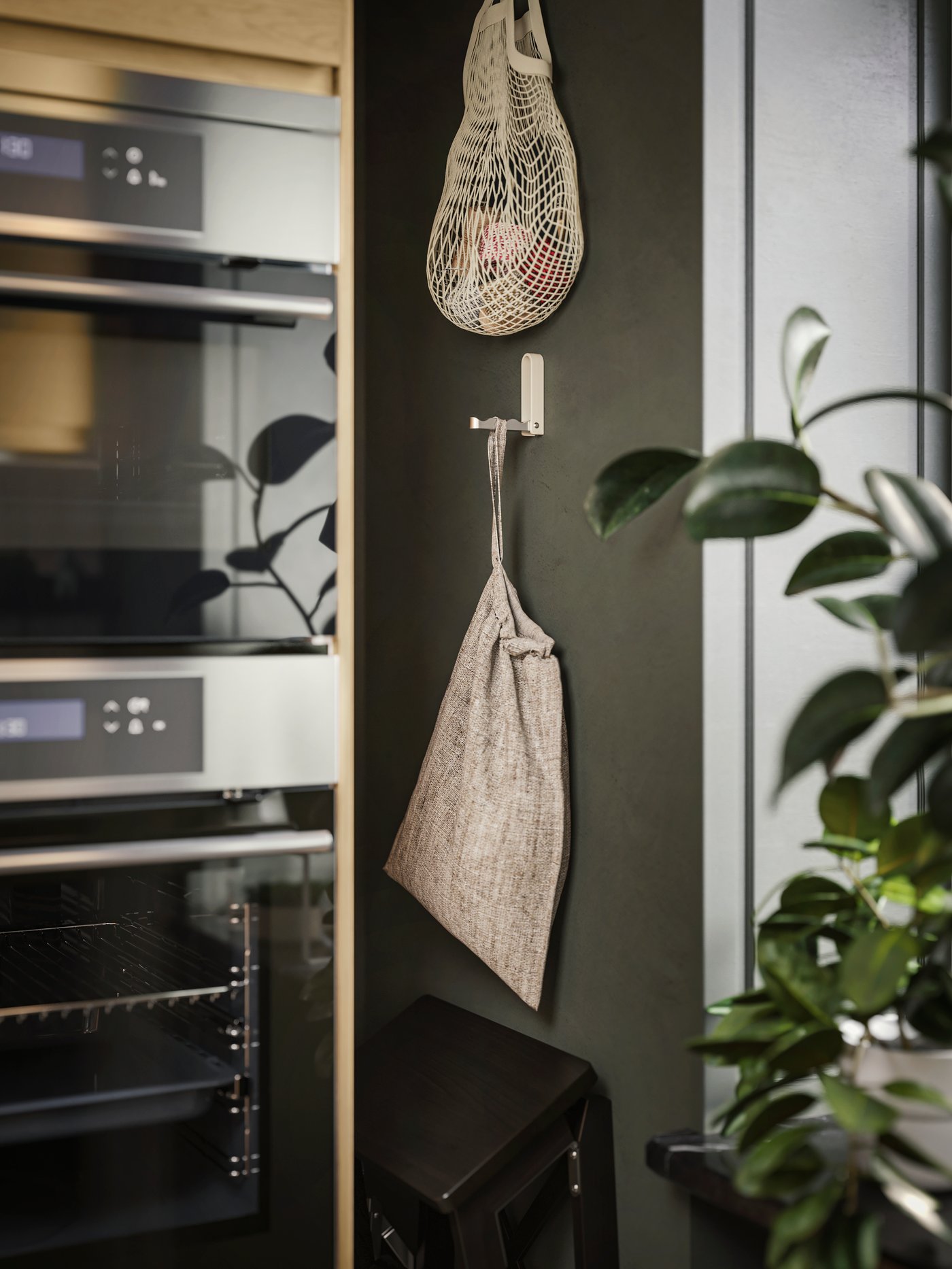 Dans une cuisine, il y a des crochets pliants KLYKET sur lesquels sont posés des sacs en filet. À côté d'eux, un four à air pulsé et un micro-ondes.