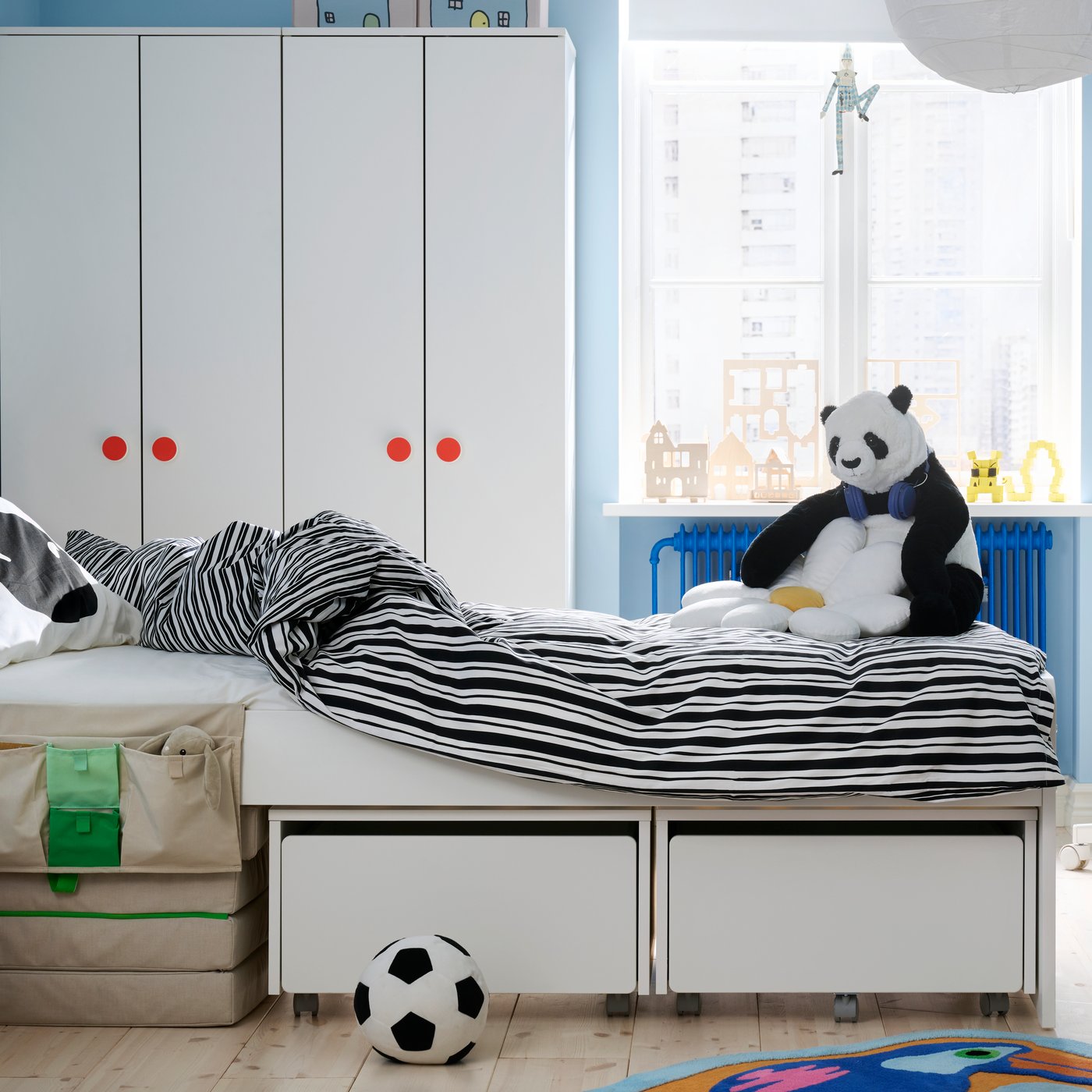 Na środku pokoju dziecięcego stoi łóżko SLÄKT zaścielone pościelą NATTHÄGER. Za łóżkiem widać szafy i okno.