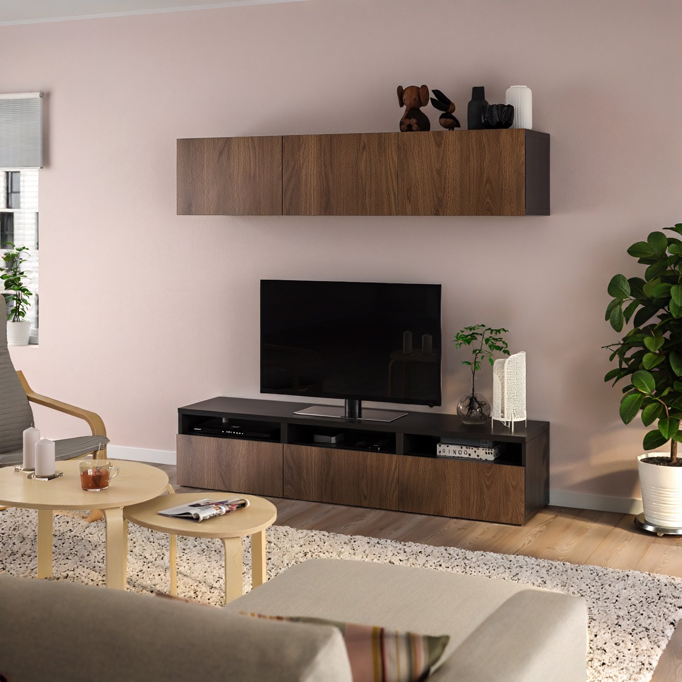 Composizione soggiorno con mobile TV BESTÅ effetto noce, contro una parete rosa chiaro in un soggiorno con divano beige e tavolini da caffè.