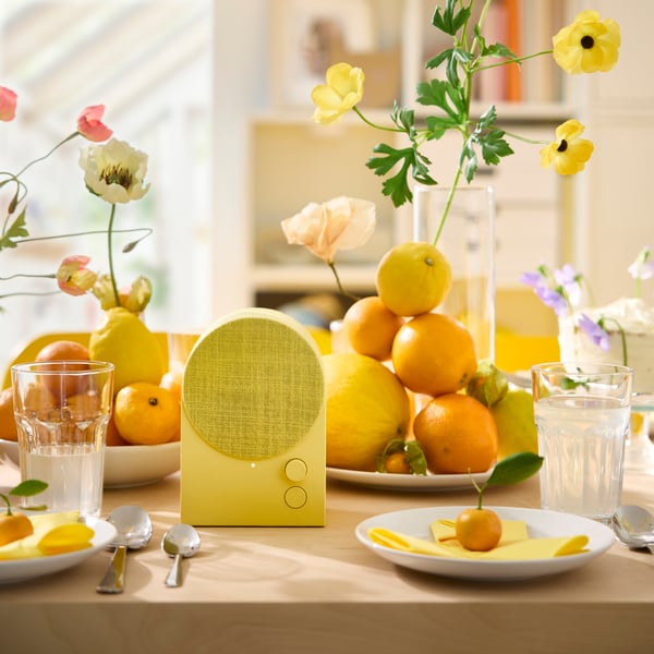 A yellow NATTBAD Bluetooth speaker is placed on a table that’s been decorated in yellow and orange for a festive party.