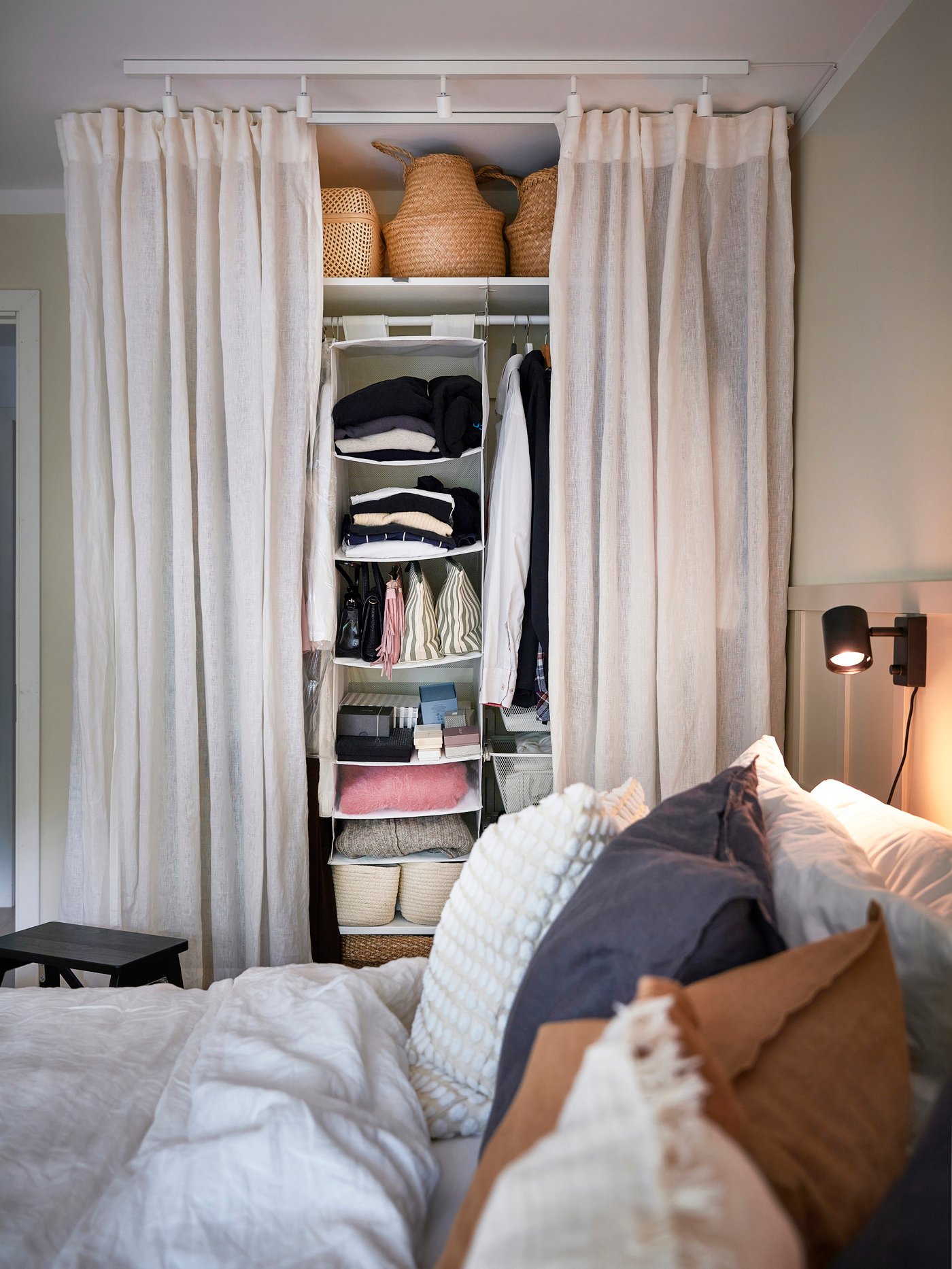 Bild på en öppen garderob med linnegardiner framför klädhyllorna.