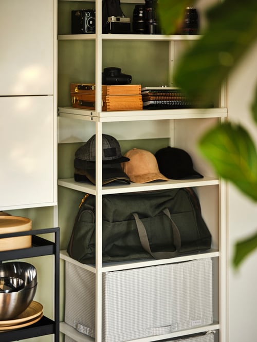 Close-up of a white, open shelving unit containing a rectangular storage case, a bag, and multiple caps.