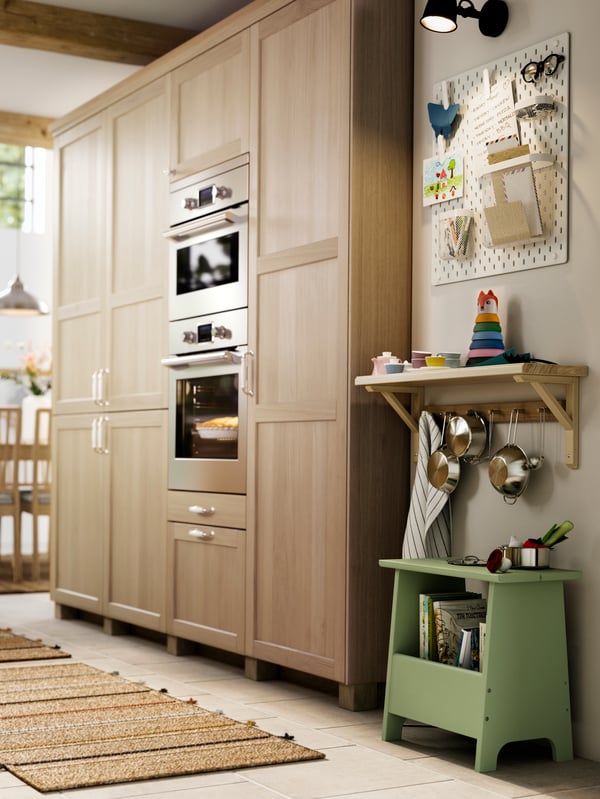 A kitchen cabinet with doors and drawers with FORSBACKA fronts in oak veneer and, next to it, a shelf with some toys.