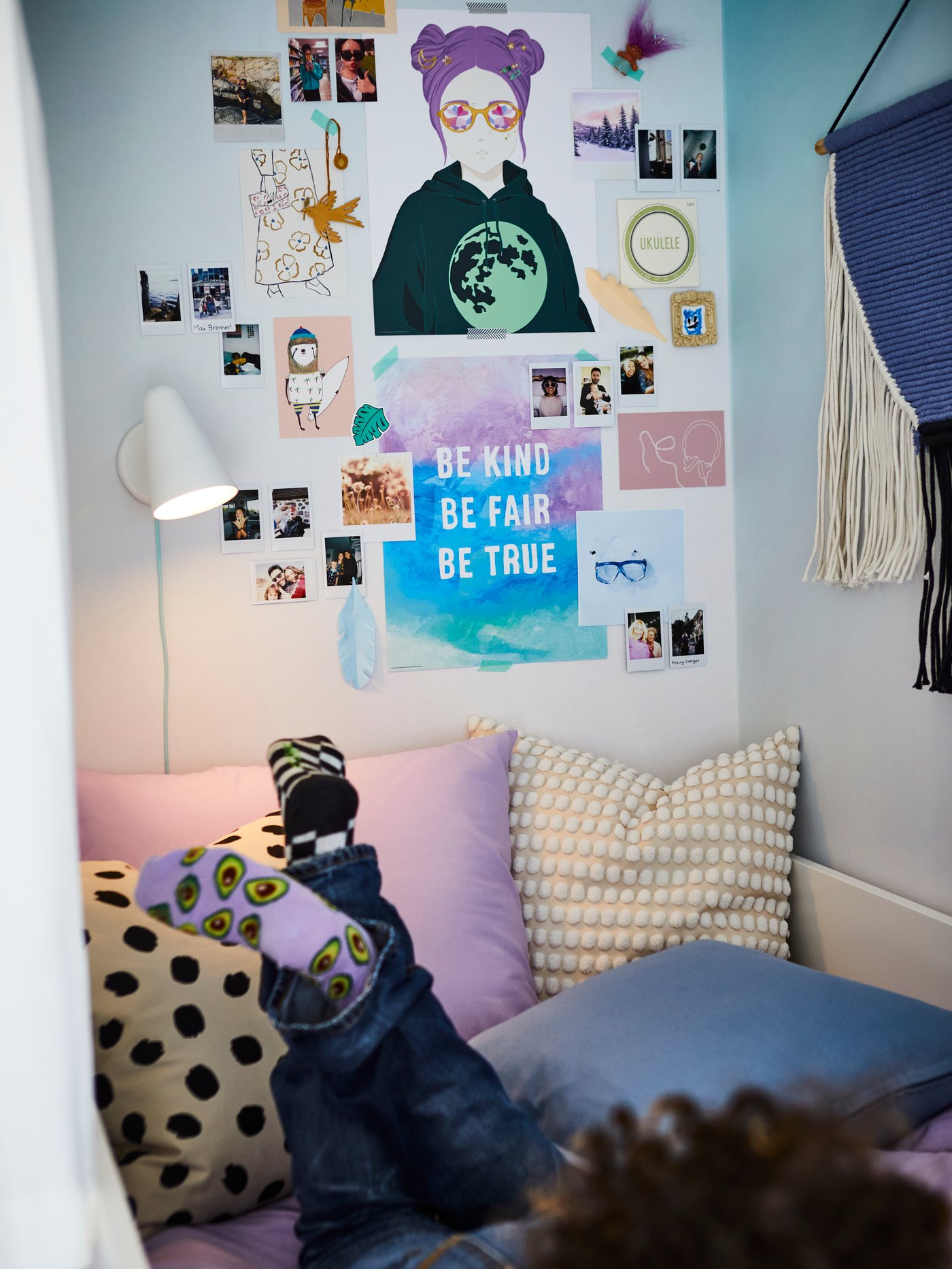A teen lies with their legs up on a bed covered in lilac NATTSVÄRMARE bed linen and cushions in ODDNY and SVARTPOPPEL covers.