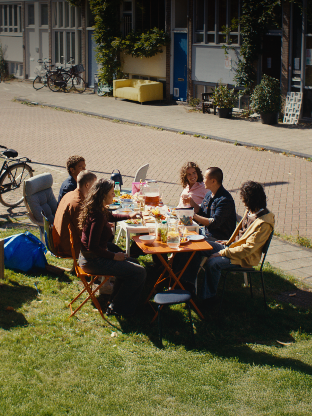 Zes personen zitten buiten aan een tafel met verschillende stoelen.