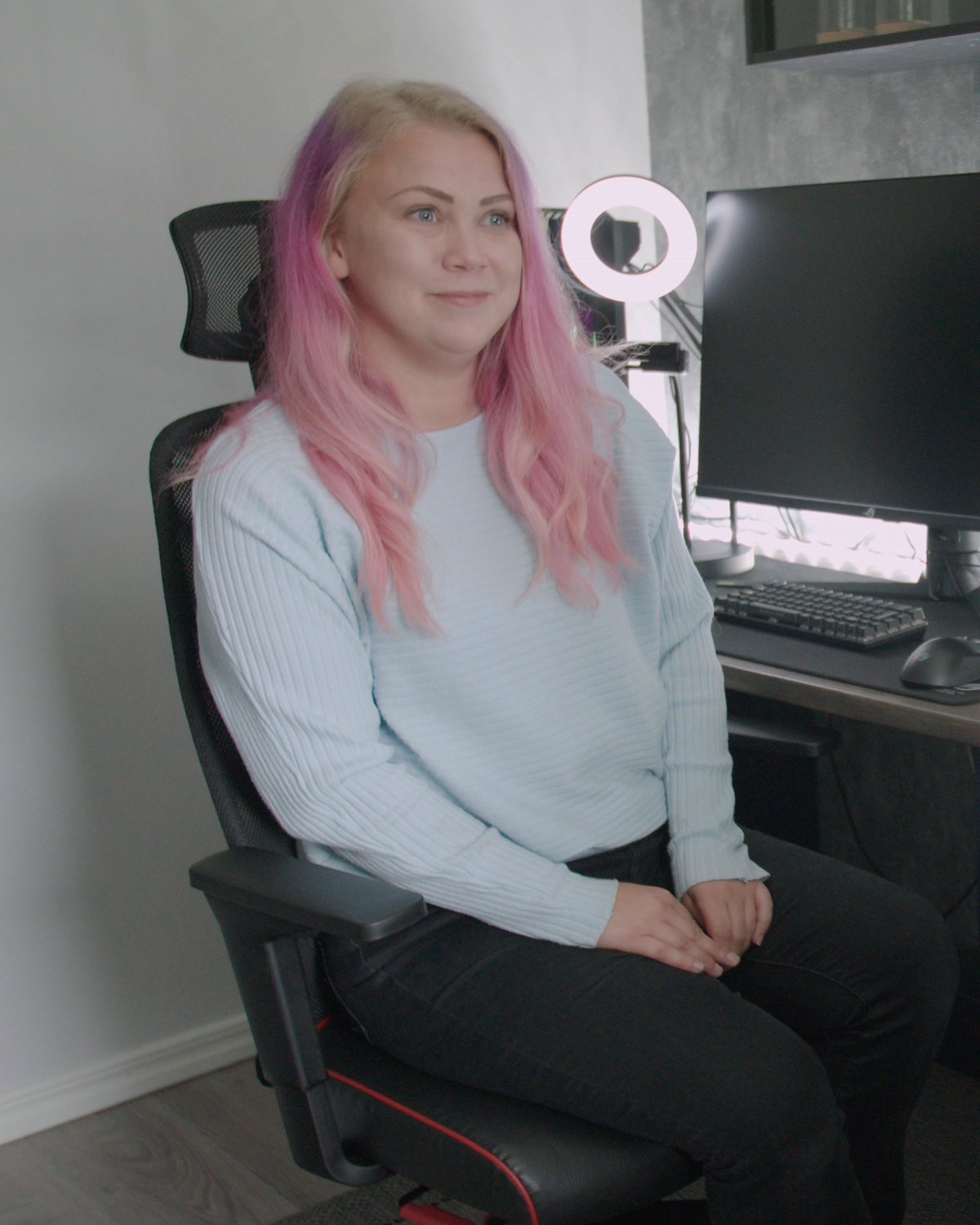 Gejmerka ružičaste kose sedi na stolici.