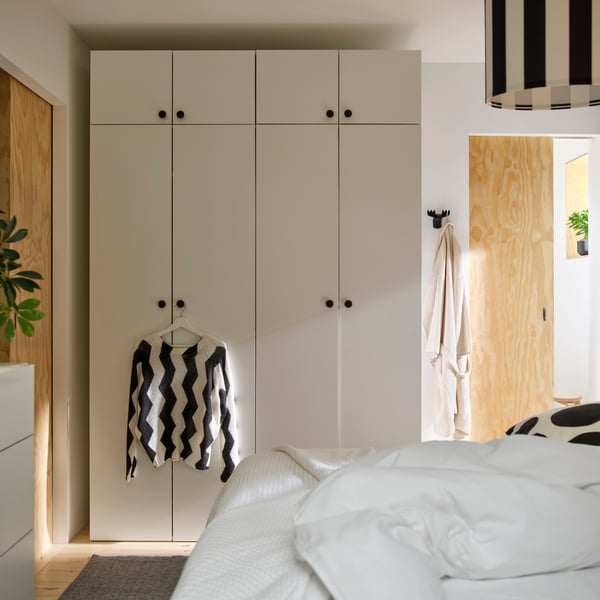 A sun-drenched bedroom with light-coloured walls and a rug, with LASTARE wardrobe combinations. A sweater hangs for the knob.