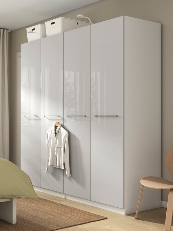 Dormitori amb un armari de portes llises en acabat brillant gris clar, dues capses d’emmagatzematge a la part superior i una camisa penjada a la porta.