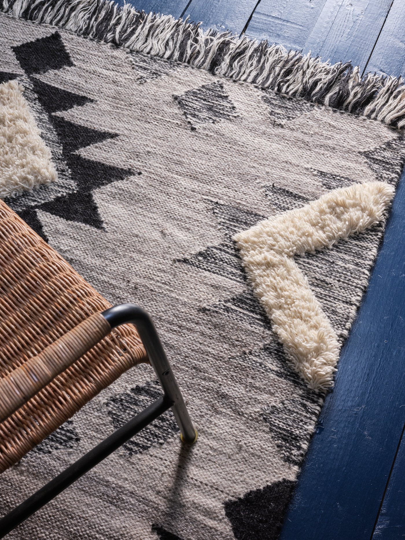 Tapete TANNISBY color gris con diseños geométricos. Se ve sobre ésta una silla de material tipo mimbre o ratán.