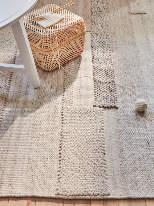 O cameră de zi modernă dotată cu un covor dreptunghiular cu fibre joase, o cutie țesută din bambus cu un capac și un scaun alb.