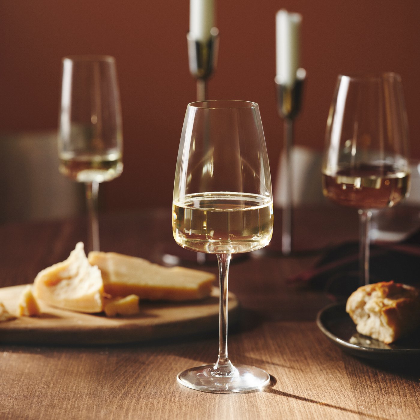 A DYRGRIP white wine glass, half filled, is standing on a wooden table next to a cheese platter and a plate with bread.