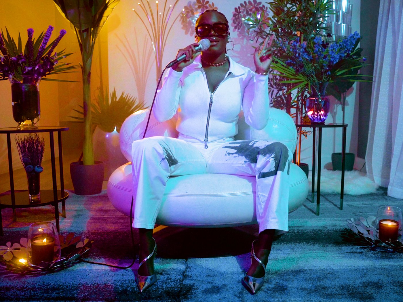 Pevačica Amaarae s mikrofonom, sedi na stolici. 