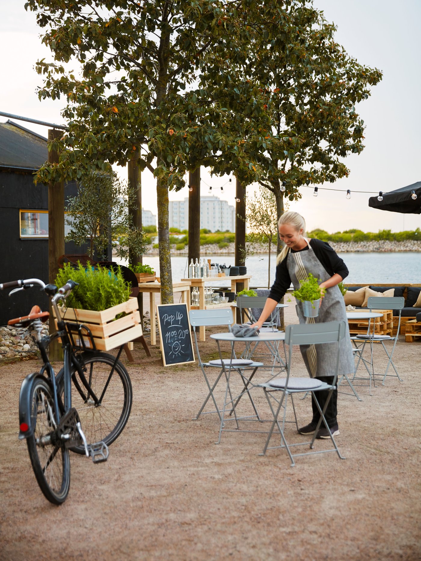 A waitress at an outdoor seating is cleaning a grey SUNDSÖ table.